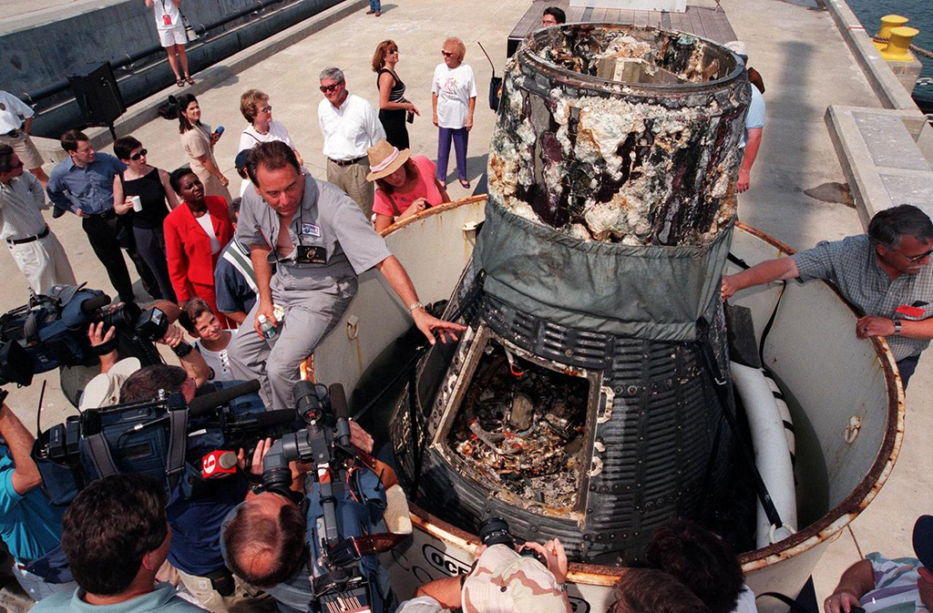Liberty Bell 7 recovered from the ocean sitting on a dock while news media surround the craft.