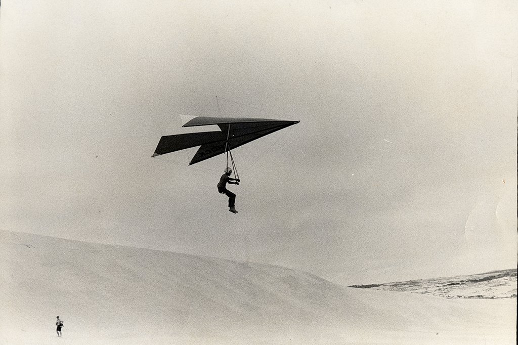 Photo of a man flying in the air over a sand dune using a glider