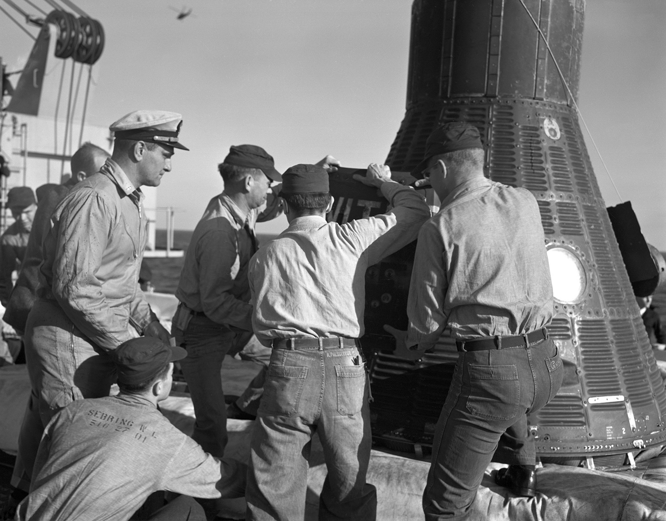 A group of men removing the hatch from a space capsule which has returned to Earth