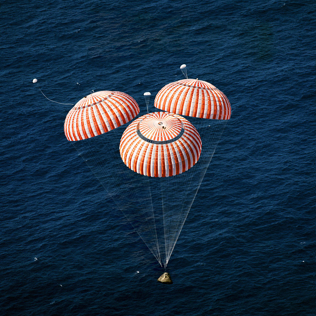 Apollo capsule falling into the ocean attached to several parachutes